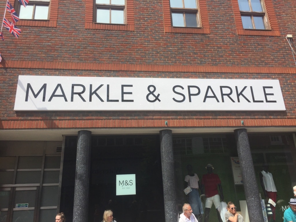 Img 1282 Brick storefront with a large white sign reading markle sparkle beneath brick windows uk flags on the left and shoppers outside