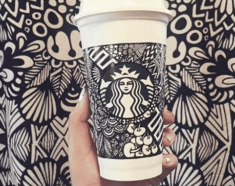Screenshot 2019 03 16 at 11 34 50 Starbucks disposable cup with a black and white ornate doodle sleeve held against a patterned background