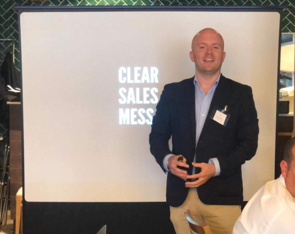 Screenshot 2023 08 11 at 23 43 55 Smiling man in a blazer presenting beside a white screen that reads clear sales mess