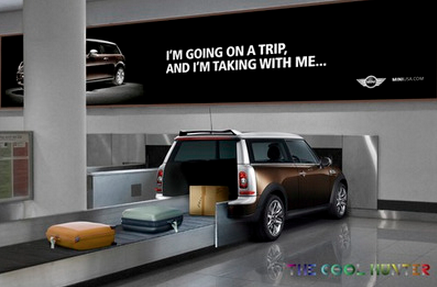 Mini car at an airport baggage claim with suitcases on a conveyor and a billboard above showing the text im going on a trip and im taking with me