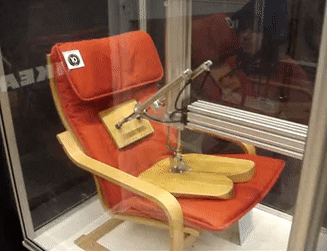 1 wtsb zefw9fbj365 e8bqw Orange padded chair with a wooden frame and built in microphone displayed behind glass in a case