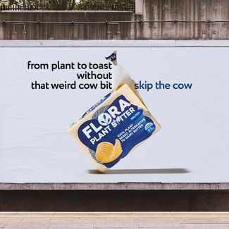 Outdoor billboard with a 3d looking flora plant butter packet appearing to fall alongside the slogan from plant to toast without that weird cow bit  skip the cow