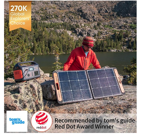 Person in a red jacket and knit hat sets up a two panel portable solar charger beside a lake with a small power station nearby award badge in corner reads 270k global explorers choice and captions show recommended by toms guide and red dot award winner