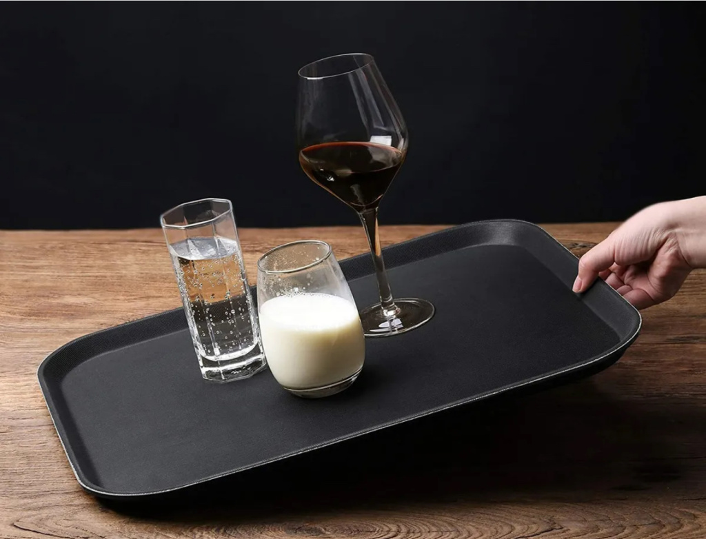 Img 0361 1 Hand placing a black serving tray on a wooden table on it are a red wine glass a milk glass and a water glass