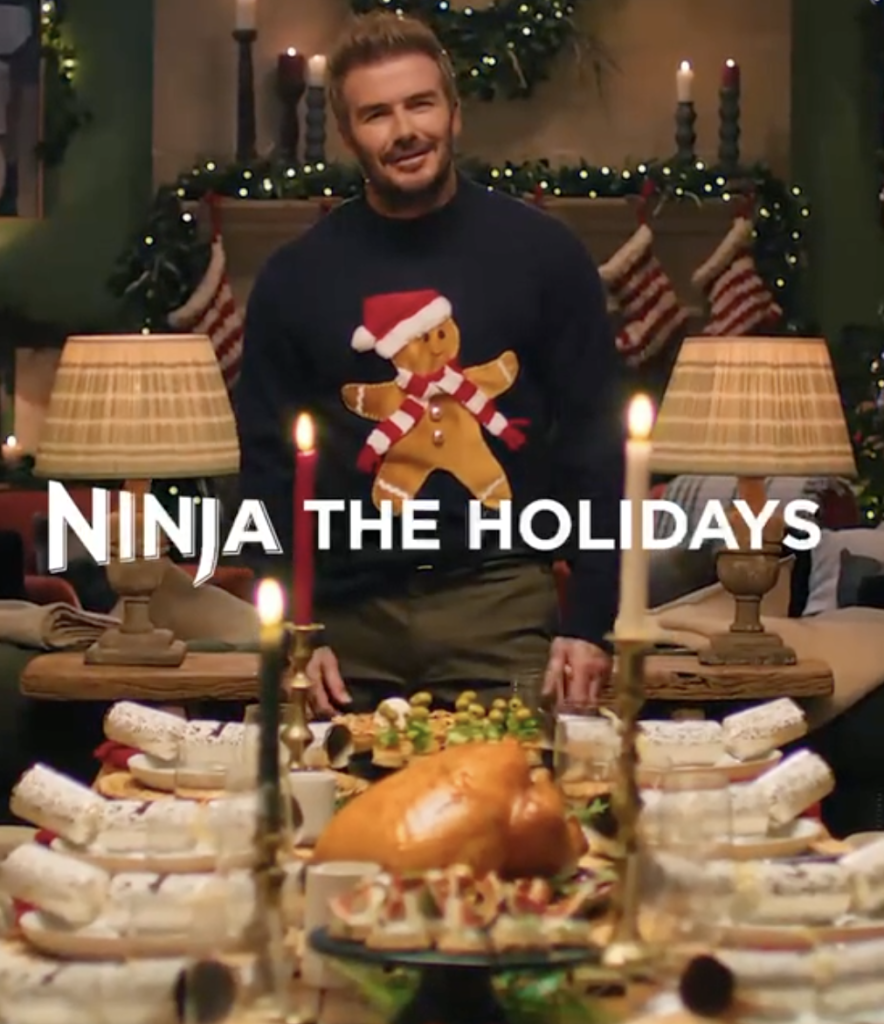 Man in a festive christmas sweater hosting a holiday feast with a long table of food and candles text overlay reads ninja the holidays