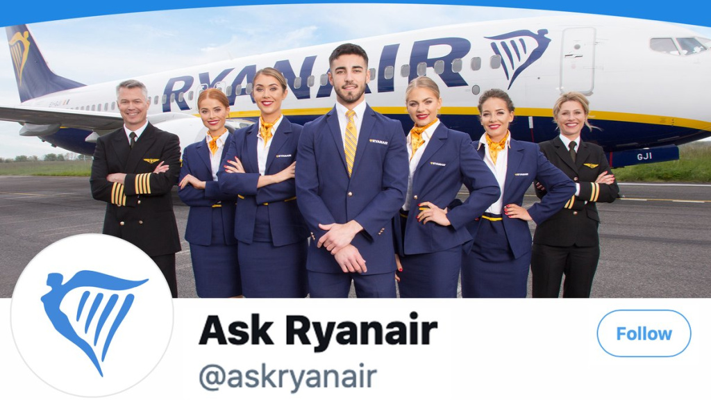 Group of ryanair crew members in navy uniforms posing in front of a ryanair airplane on the tarmac with visible branding and ask ryanair text in the foreground