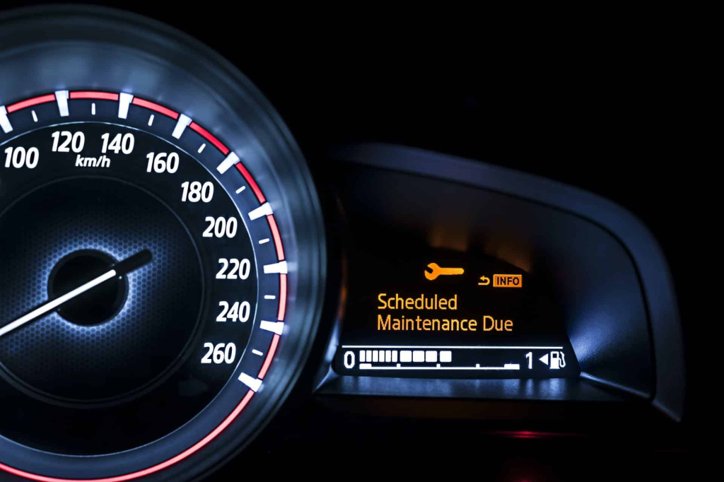 Close up of a car dashboard with a speedometer and an orange maintenance reminder reading scheduled maintenance due