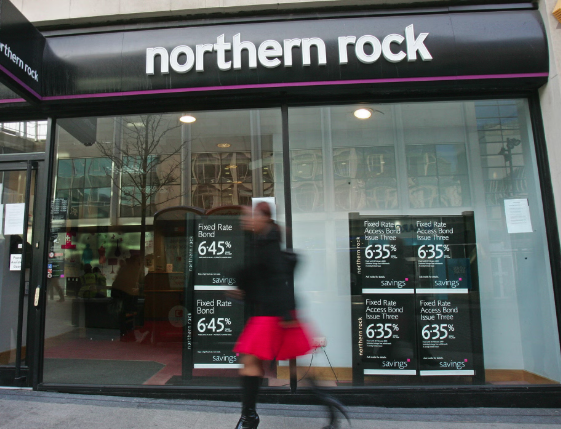 Screenshot 2025 03 24 at 21 59 23 Northern rock bank storefront with a large sign window posters advertise fixedrate bond savings showing rates around 6 4 as a person passes by