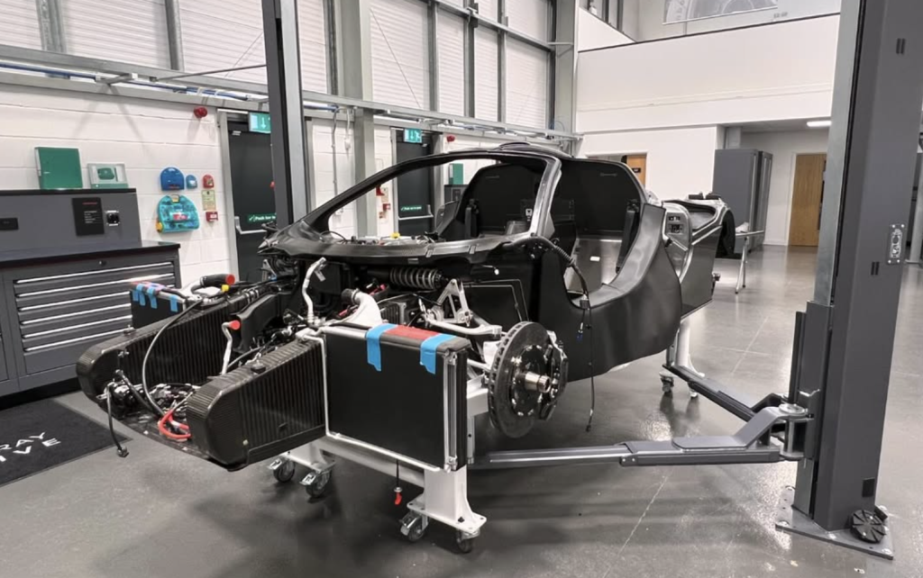 Sports car chassis on a rolling stand in a modern workshop with the front end disassembled and exposed radiator and engine components