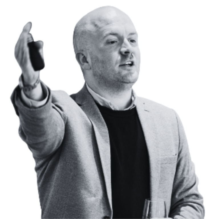 James presenting no background 768x768 Male presenter in a blazer raising a wireless microphone toward the audience while speaking