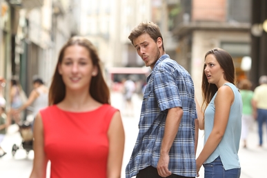 Man in a blue plaid shirt glances over his shoulder at two women walking on a busy city street