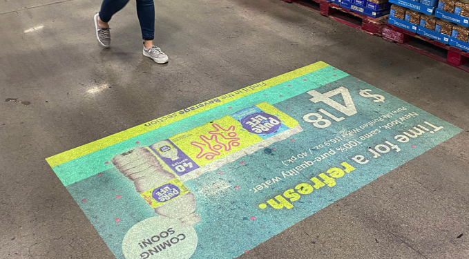 Colorful floor advertisement painted in a supermarket aisle with images of ice cream cones and a slogan and a person walking past in sneakers