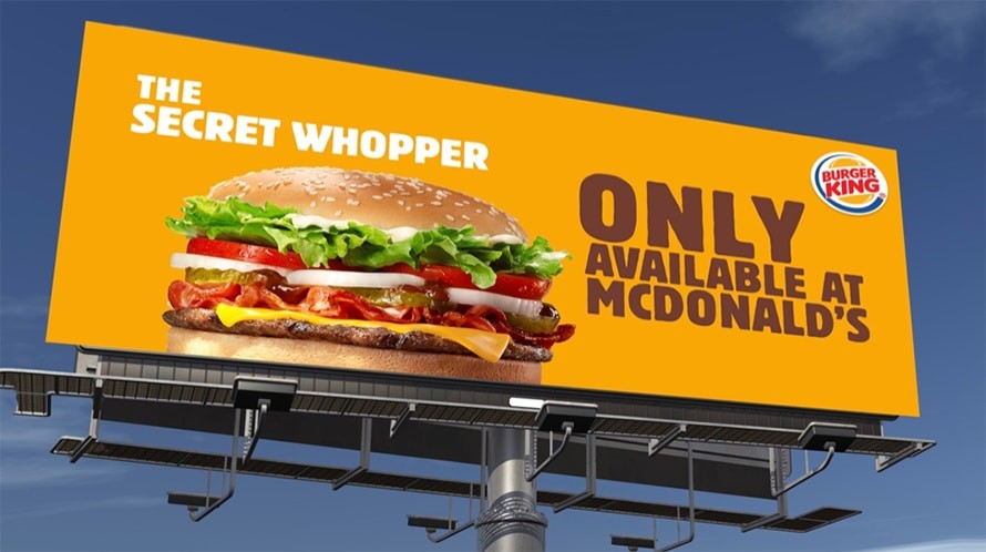 Bright orange burger king billboard with a large cheeseburger and the text the secret whopper and only available at mcdonalds
