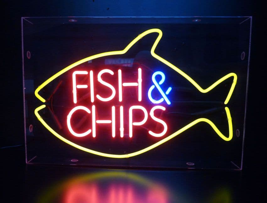Neon sign advertising fish  chips with a yellow fish outline and red lettering on a dark background