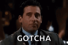 Smirking man in a dark suit with the word gotcha overlaid implying a playful catch or prank
