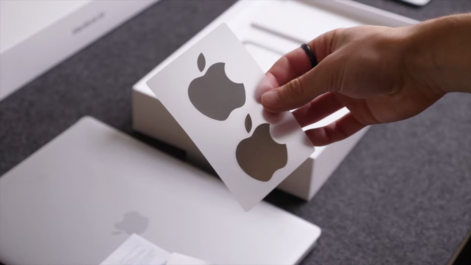 Hand peels a white apple logo sticker from a sheet during unboxing with a box in the background
