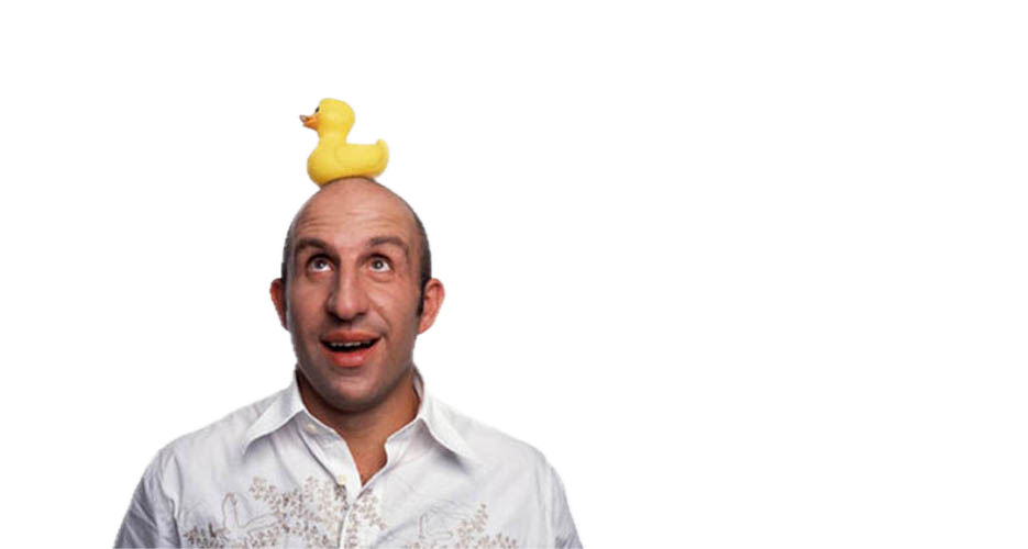 Man with a yellow rubber duck perched on his bald head looking up with a surprised expression on a dark background