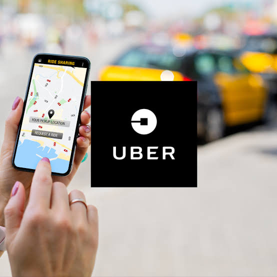 Smartphone screen shows a ridehailing map with pickup location uber logo sits over the image blurred city street in the background