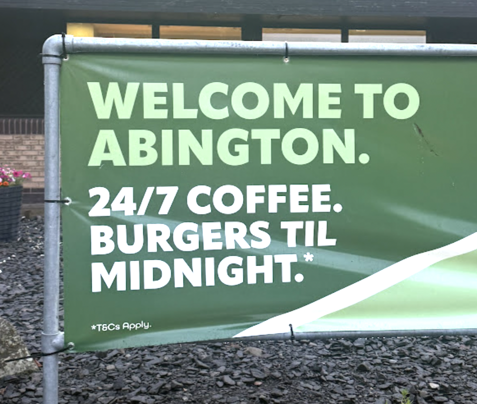 Green outdoor banner that says welcome to abington 247 coffee Burgers til midnight  with a white diagonal swoosh and metal frame