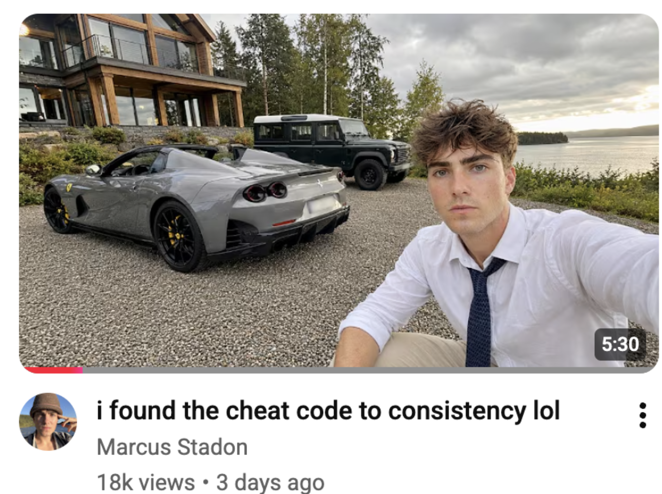 Young man taking a selfie beside a gray ferrari parked on a gravel driveway near a modern wooden house with a lake in the background