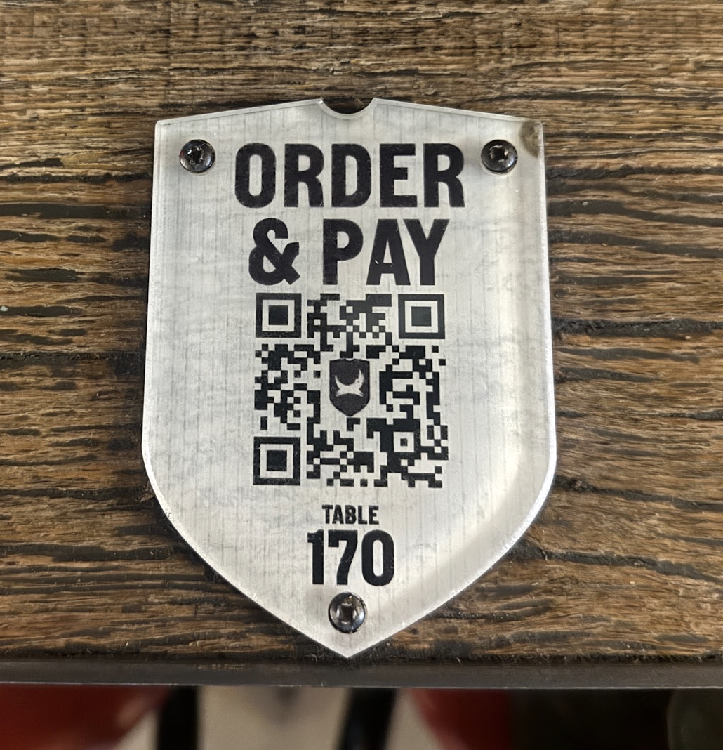 Metal shield sign reading order  pay with a qr code and table 170 at bottom on a wooden table surface