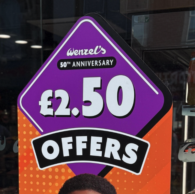 Promotional sign for wenzels 50th anniversary £2 50 offers on a purple diamond with orange accents in a shop window